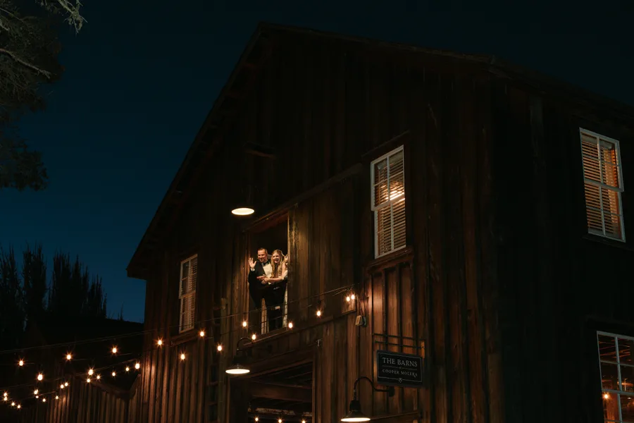 Luke and Jessica waving from a balcony window at The Barns at Cooper Molera, Monterey, at night